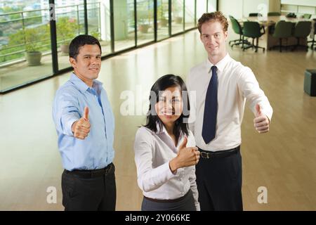 Eine glückliche Gruppe von drei verschiedenen Geschäftsleuten zeigt jeweils einen fröhlichen Daumen nach oben, um die Genehmigung zu erhalten Stockfoto