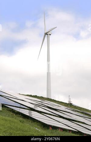 Sonnenkollektor und Windmühle vor einem Baum und blauem Himmel Stockfoto