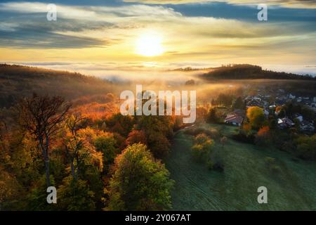Sonnenaufgang über Schichten von goldenem Nebel in einer idyllischen ländlichen Landschaft. Mit herbstlichen Farben auf den Bäumen und goldenen beleuchteten Wolken und Nebel Stockfoto