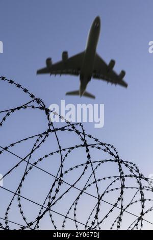 Symbolisches Bild, Abschiebungsflüge illegaler und krimineller Migranten, Bild eines fliegenden Flugzeugs über Stacheldraht im Sonnenuntergang, symbolisiert Freiheit Stockfoto