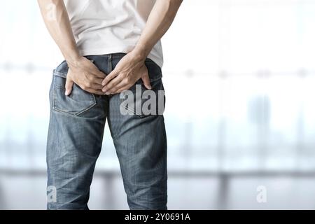 Ein Mann, der seinen Hintern vor Schmerzen in blauem Hintergrund hält Stockfoto