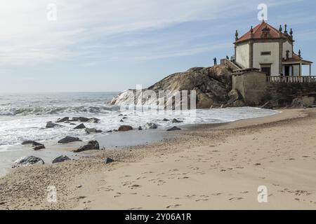 Felsen in der Brandung, Sandstrand und Wahrzeichen Capela do Senhor da Pedra, historische Kapelle auf einem Felsen am Praia do Senhor da Pedra, Gulpilhares, Vila Nova de Stockfoto