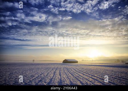 Hütte bei Sonnenaufgang, Winter mit Schnee und leichtem Dunst in Kombination mit einem dunkelblauen Himmel, auf diesem sind schöne Cumulus Wolken Stockfoto