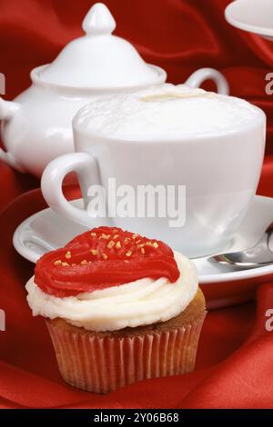 Romantisches Valentinstag-Frühstück mit Cupcake, rotem Buttercremeherz und Cappuccino. Im Hintergrund eine Zuckerschale. Selektiver Fokus Stockfoto