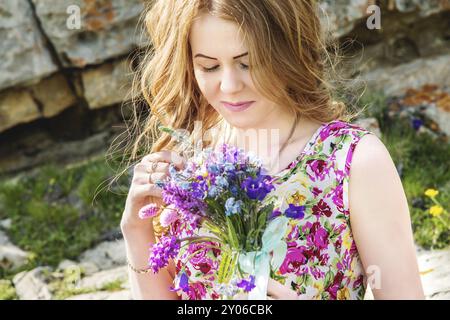 Nahporträt eines rustikalen Mädchens. Ein Mädchen in einem bunten Kleid hält einen Blumenstrauß. Schnüffelnde Blumen Stockfoto