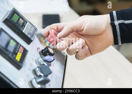 Nahaufnahme der Hand eines Mannes auf einer roten Taste auf dem Bedienfeld. Not-aus oder Start der Anlage und Produktion Stockfoto