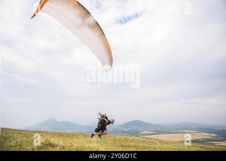 Ein Mann Gleitschirm, der vom Rand des Berges mit Feldern im Hintergrund abheben. Gleitschirmfliegen Stockfoto