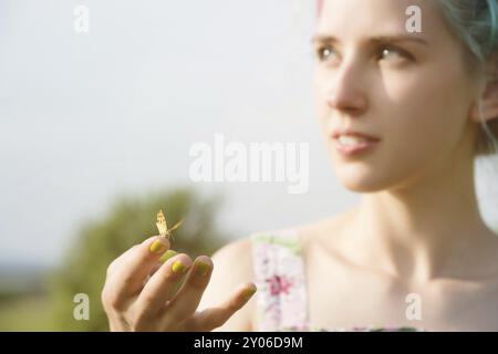 Porträt einer schönen Frau, die einen Schmetterling auf der Hand im Garten hält. Schönheitsporträt. Einheit mit der Natur. Ökologie Konzept Stockfoto