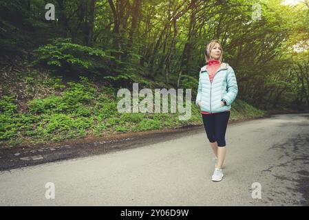 Porträt eines attraktiven Sportmädchens in einer leichten Daunenjacke, die bluetooth-Kopfhörer mit Musik oder Naturgeräuschen anzieht Stockfoto