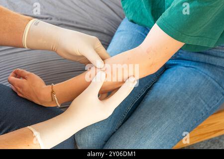 Doktor in Plain Clothes, der den Arm einer Frau behandelt. Häusliche Pflege für ein Mädchen. Arzt ohne weißen Mantel mit weißen Handschuhen, die häusliche Pflege medizinische Behandlung geben. Stockfoto