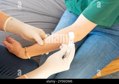 Doktor in Plain Clothes, der den Arm einer Frau behandelt. Häusliche Pflege für ein Mädchen. Arzt ohne weißen Mantel mit weißen Handschuhen, die häusliche Pflege medizinische Behandlung geben Stockfoto