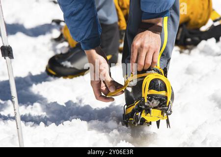 Ein junger Wanderer zieht Klettersteige über Bergschuhe, um auf einem Gletscher und gefrorenem Schnee zu spazieren Stockfoto