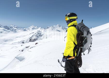 Ein Bergsteiger hält eine Eisaxt hoch in den Bergen, die mit Schnee bedeckt sind. Blick von hinten. Outdoor Extremklettersport im Freien mit Bergsteigen Stockfoto