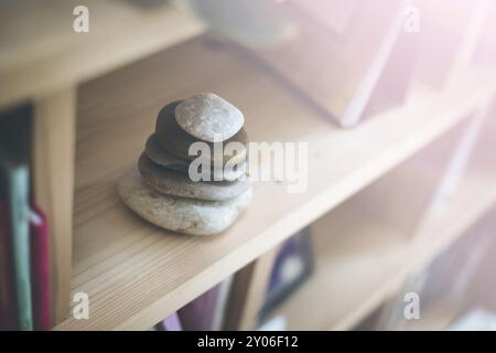 Feng Shui: Steinkairn zu Hause in einem Bücherregal, verschwommene Bücher im Vorder- und Hintergrund. Balance und Entspannung. Sonnenlicht Stockfoto