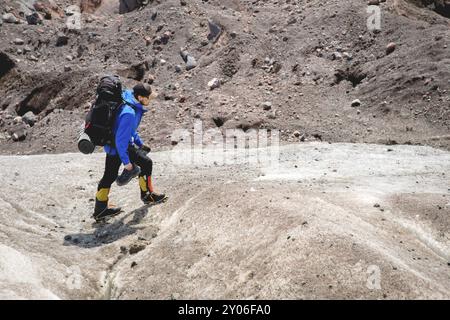 Ein Bergsteiger mit Rucksack läuft in Steigeisen entlang eines staubigen Gletschers mit Gehwegen in den Händen zwischen Rissen im Berg Stockfoto