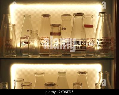 Auswahl an Vintage-Glasmilchflaschen mit Namen oder Namen von Molkereien oder Molkereien, hintergrundbeleuchtet im Vitrine. Themen: Milchlieferung, Milchrunde. Stockfoto