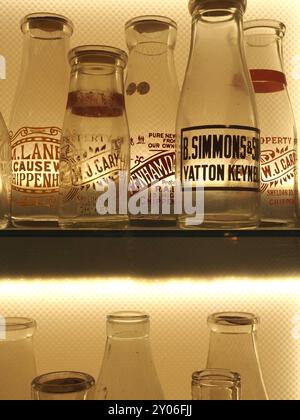 Auswahl an Vintage-Glasmilchflaschen mit Namen oder Namen von Molkereien oder Molkereien, hintergrundbeleuchtet im Vitrine. Themen: Milchlieferung, Milchrunde. Stockfoto