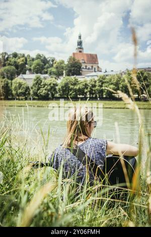 Schöne junge Mädchen sitzt an einem Fluss und spielt Ihre Westerngitarre Stockfoto