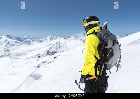 Ein Bergsteiger hält eine Eisaxt hoch in den Bergen, die mit Schnee bedeckt sind. Blick von hinten. Outdoor Extremklettersport im Freien mit Bergsteigen Stockfoto