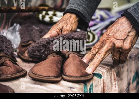 Alte faltige Frauenhände halten Kinderschuhe auf dem Flohmarkt im Kaukasus Stockfoto