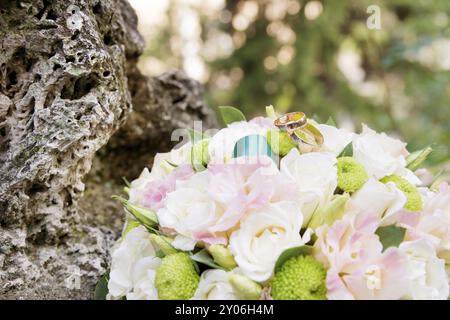 Hochzeitsgoldringe liegen auf einem Hochzeitsstrauß, der aus blauen violetten und weißen Blumen besteht Stockfoto