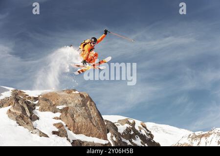 Ein Skirennläufer springt von hohen Felsen in den Bergen. Flusspulver aus dem Schnee hinter dem fliegenden Athleten Stockfoto