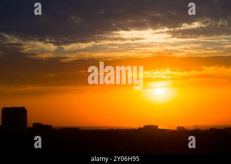 Sonnenaufgang in einem bewölkten Himmel über einer Küstenstadt. Die Sonne bricht durch die Wolken über den Dächern. Silhouetten von Gebäuden und Schiffen vor Anker Stockfoto