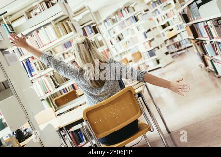 Müde Studentin sitzt am Schreibtisch mit einem Stapel Bücher, Universitätsbibliothek Stockfoto