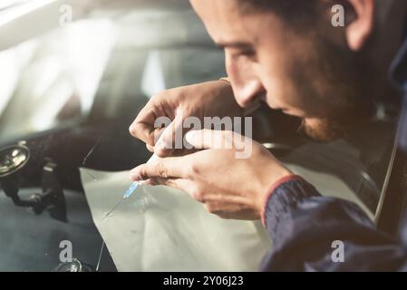 Nahaufnahme eines professionellen Windschutzscheibenreparateurs füllt einen Riss im Glas mit einem speziellen Polymer durch eine Spritze. Beseitigung von Rissen und Spänen o Stockfoto