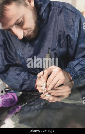 Nahaufnahme von Autoverglasungsarbeitern, die eine Windschutzscheibe oder Windschutzscheibe eines Autos an einer Werkstattwerkstatt reparieren und reparieren. Bohren Sie das Glas für die Reparatur Stockfoto