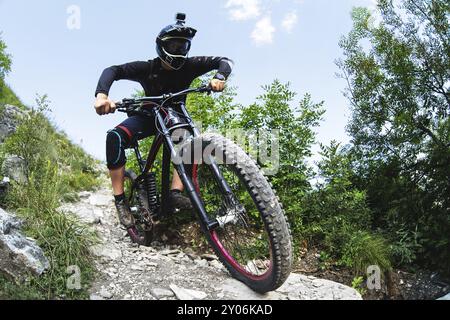 Ein junger Fahrer auf einem Fahrrad, der bergab fährt, steigt die Felsen im Wald ab Stockfoto