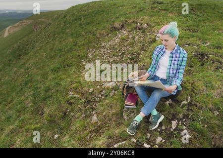 Mädchen mit mehrfarbigem Haar, das auf einer Naturlesekarte sitzt und einen Kompass in der Hand hält. Das Konzept der Navigation in der Suche und Tourismus i Stockfoto