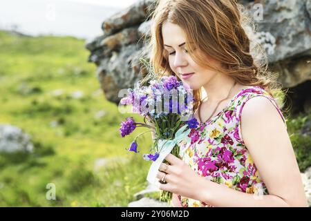 Nahporträt eines rustikalen Mädchens. Ein Mädchen in einem bunten Kleid hält einen Blumenstrauß. Schnüffelnde Blumen Stockfoto