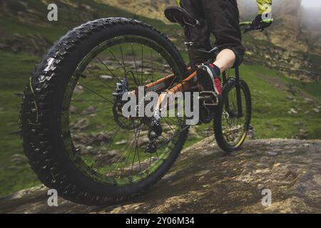 Beine des Radfahrers und Hinterrad Nahaufnahme des hinteren MTB-Bikes in den Bergen vor dem Hintergrund von Felsen bei nebeliger Witterung. Das Konzept der extremen spor Stockfoto