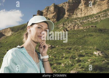 Fitness-Läuferin, die Musik über die Natur hört. Porträt eines schönen Mädchens mit Ohrhörern und Laufkappe. Vor dem Hintergrund von Stockfoto