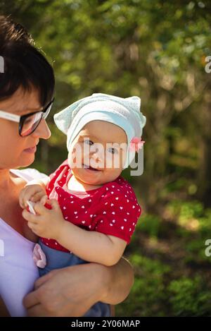 Ein Gefühlsbild eines einjährigen Babys und ihrer Mutter, die sich im sonnigen Sommerwald glücklich fühlen Stockfoto