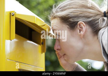 Die junge Frau schaut neugierig in einen Briefkasten Stockfoto