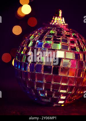 Nahaufnahme von einem bunten disco Weihnachtskugel auf einem Holztisch, verschwommenes Weihnachtsbaumbeleuchtungen im Hintergrund, schönes Bokeh Stockfoto