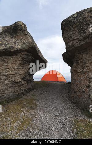 Ein orangenes Zelt steht hoch in den Bergen zwischen zwei hohen Felsen, die Steinpilze im Kaukasus genannt werden. Berg Elbrus Stockfoto