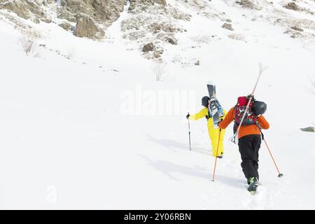 Zwei Ski Freerider klettern die Piste in Tiefschneepulver, wobei die Ausrüstung auf der Rückseite auf dem Rucksack befestigt ist. Das Konzept des Winterextremen Sports Stockfoto