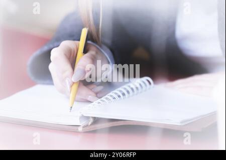 Nahaufnahme der Hand einer Studentin in einem Café hinter dem Glas mit einer Reflexion, die etwas mit einem Kugelschreiber in ein Notizbuch schreibt. Dekontrast Stockfoto