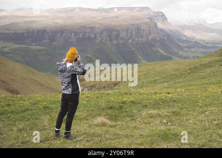 Ein junges Mädchen fotografiert an einem bewölkten Tag ein Plateau auf einem hohen Berg. Blick auf das Mädchen dahinter Stockfoto