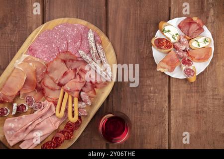 Verkostung Von Wurstwaren. Ein Foto über dem Kopf von vielen verschiedenen Würstchen und Schinken, Aufschnitt, von oben auf einem dunklen rustikalen Hintergrund mit einem Glas r Stockfoto