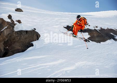 Ein Skirennläufer springt von hohen Felsen in den Bergen. Flusspulver aus dem Schnee hinter dem fliegenden Athleten Stockfoto