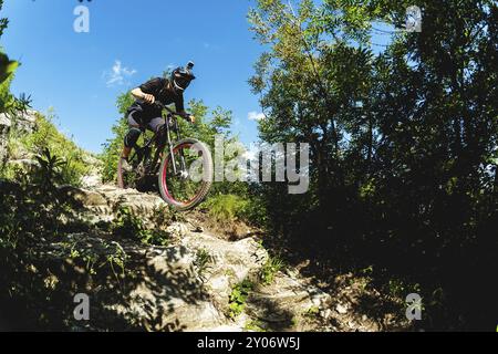 Ein junger Fahrer auf einem Fahrrad, der bergab fährt, steigt die Felsen im Wald ab Stockfoto