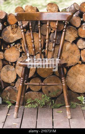 Alter Vintage Stuhl aus Holz auf dem Hintergrund von Holzscheite Brennholz Stockfoto