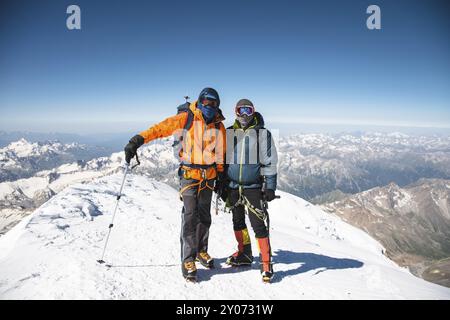 Portrait Eines Kletterers mittleren Alters in einer Daunenjacke, der neben seinem Freund auf dem Weg zum Gipfel eines schneebedeckten Berges steht. Der Begriff Rest Stockfoto