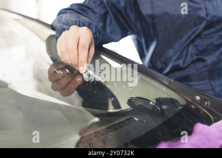 Nahaufnahme von Autoverglasungsarbeitern, die eine Windschutzscheibe oder Windschutzscheibe eines Autos an einer Werkstattwerkstatt reparieren und reparieren. Bohren Sie das Glas für die Reparatur Stockfoto