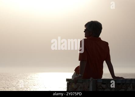 Frau, die in der Abendsonne am Meer sitzt Stockfoto