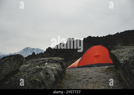 Ein orangenes Zelt steht hoch in den Bergen zwischen zwei hohen Felsen, die Steinpilze im Kaukasus genannt werden. Berg Elbrus Stockfoto